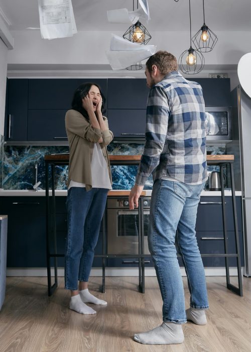A couple arguing in a modern kitchen, surrounded by flying papers. Emotionally tense moment.